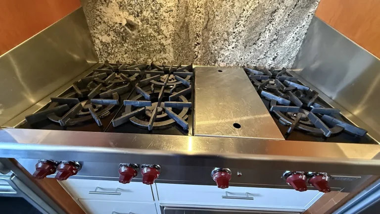 Stainless gas rangetop with red knobs and a center griddle