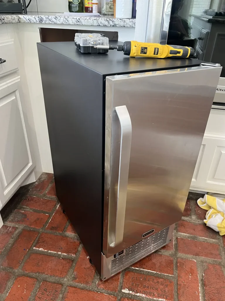 Stainless undercounter ice machine pulled out for service on a brick floor