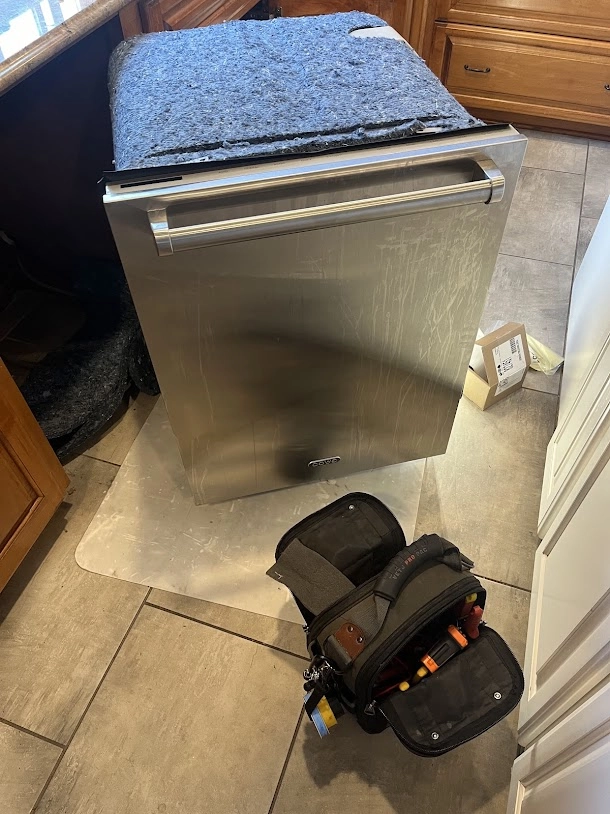 Stainless Cove dishwasher pulled out beside a technician's tool bag.