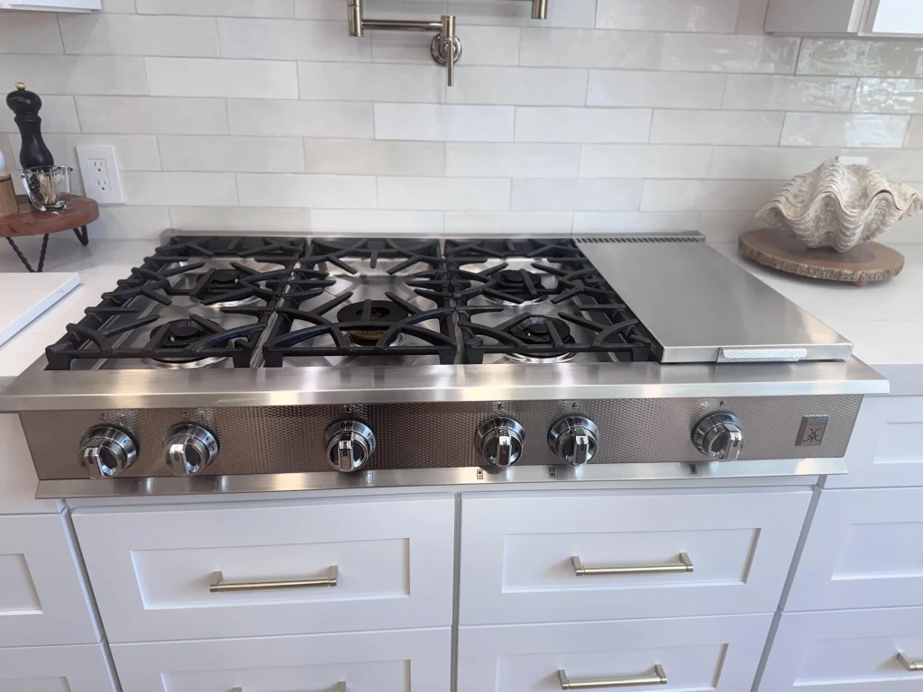 Stainless Hestan gas rangetop with six burners and control knobs.