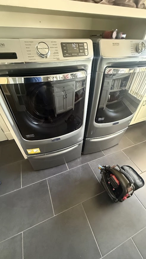 Gray Maytag front load washer and dryer with a tool bag nearby.