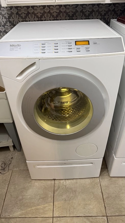 White Miele front load washing machine in a laundry area.