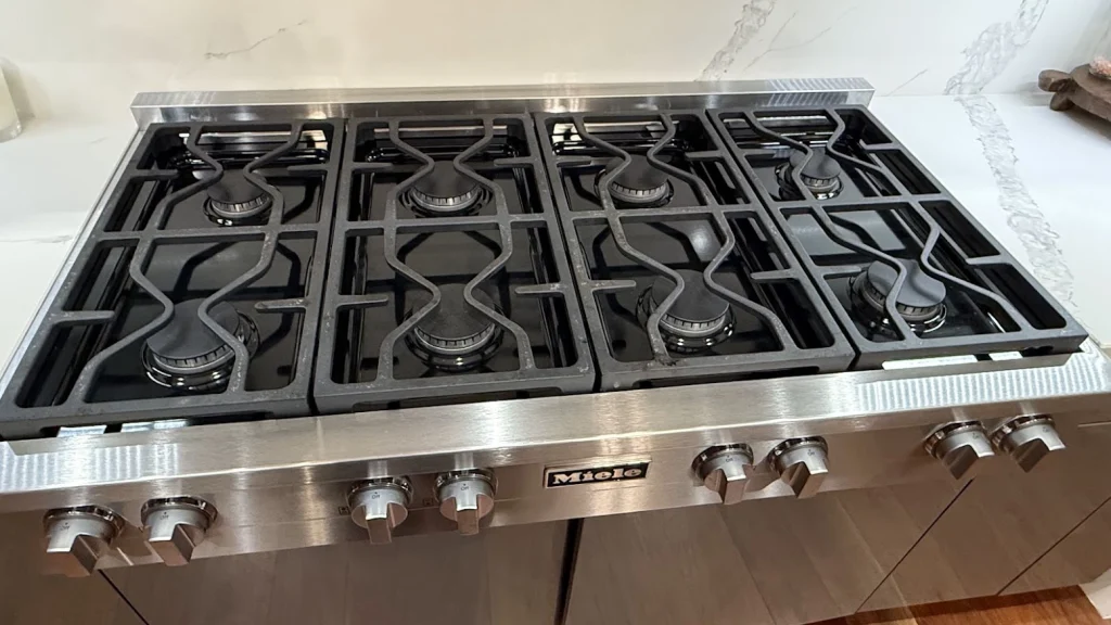 Stainless Miele gas cooktop with six burners and front control knobs.
