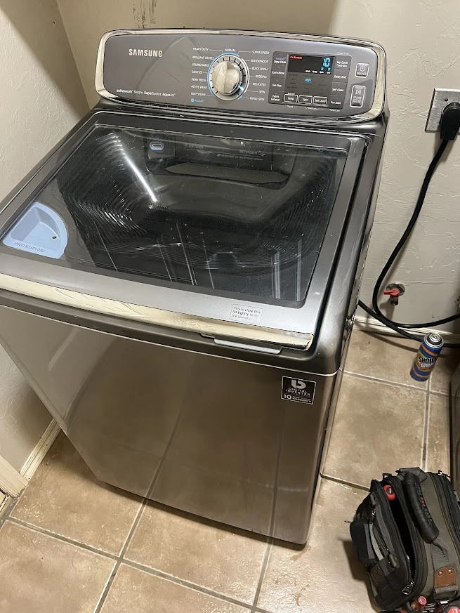 Gray Samsung top load washer with lid closed and tool bag nearby.