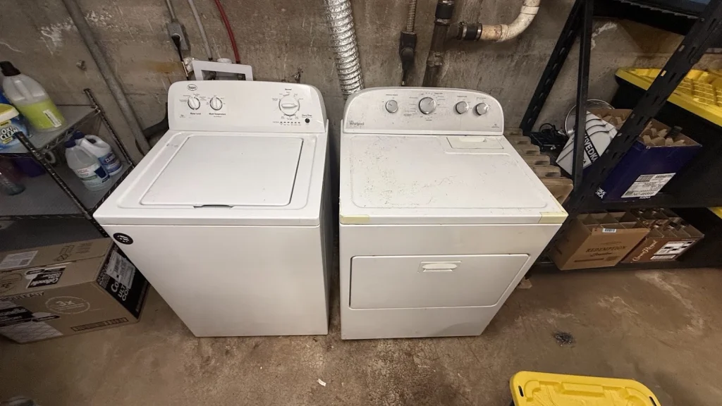 Two white Whirlpool top load washers in a utility room.