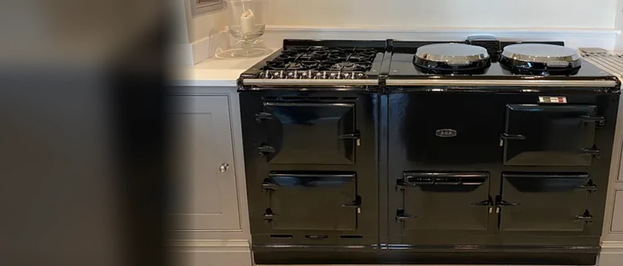 Black AGA cooker with hotplate lids and cast-iron oven doors in a white kitchen