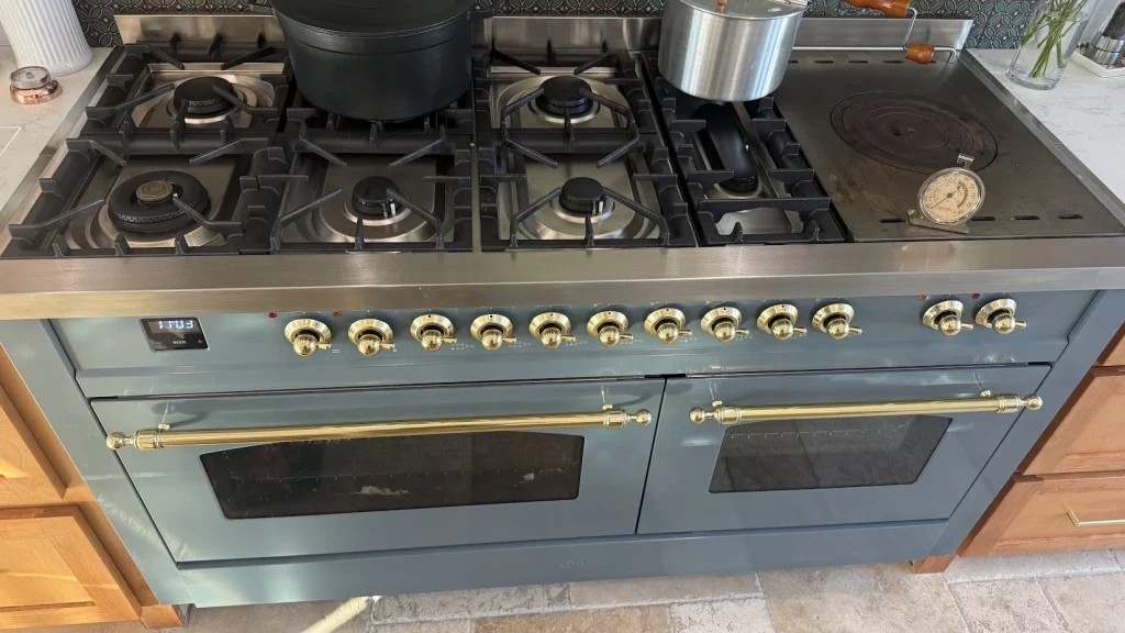 Blue gas range with two ovens installed between kitchen cabinets.
