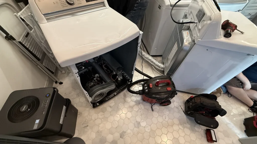 Washer and dryer with panels removed and tools on the floor.