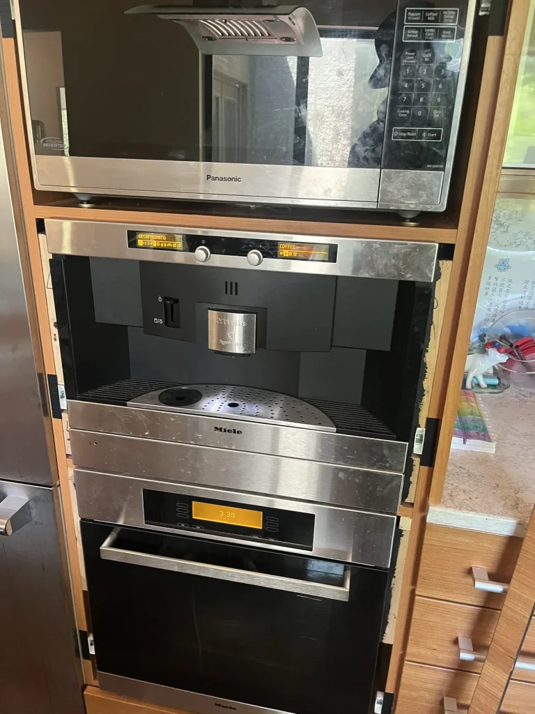Miele built-in coffee system, steam oven and wall oven stacked in a wood cabinet
