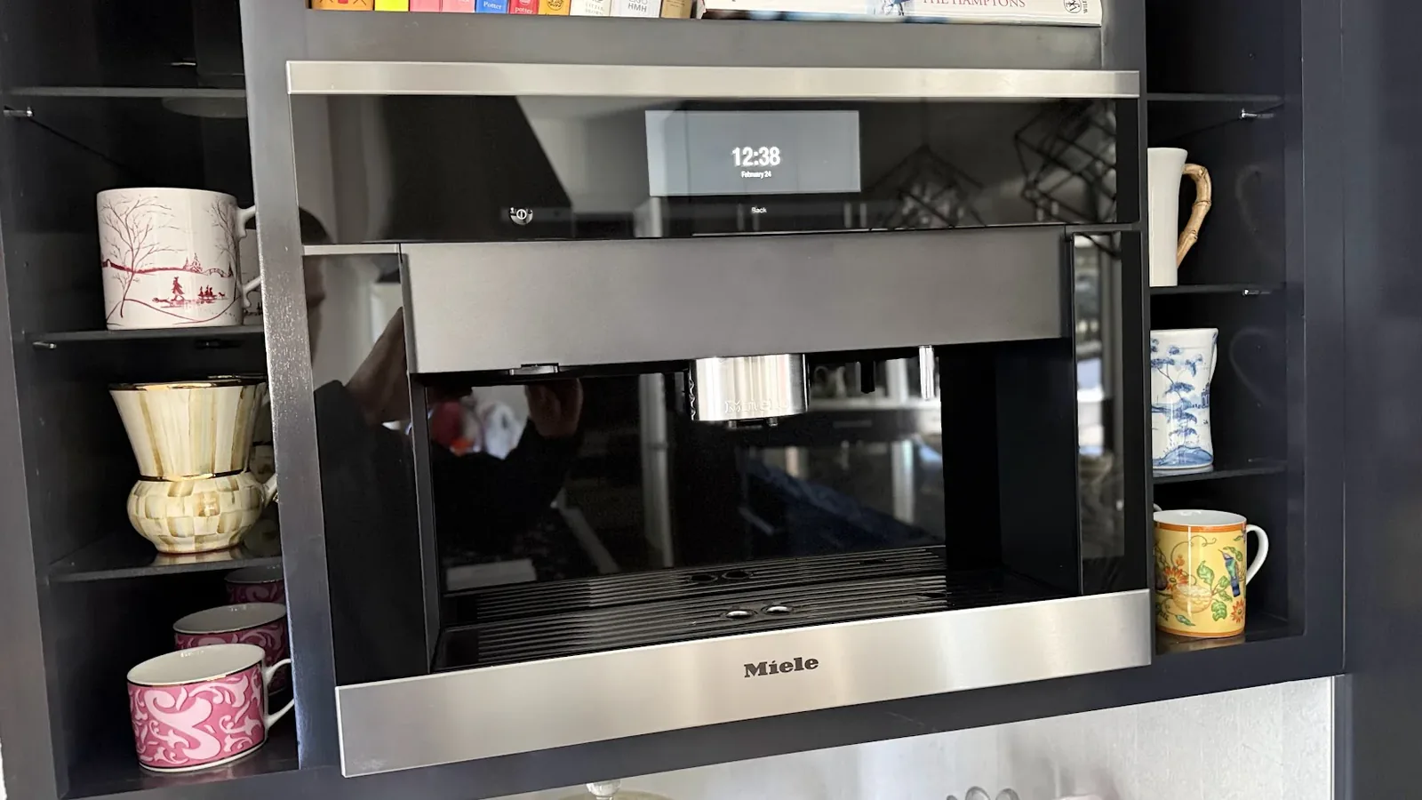 Miele built-in coffee system in dark cabinetry with mugs on open shelves