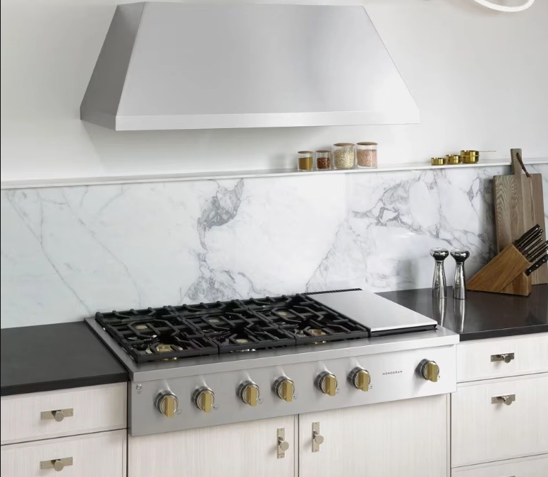 Monogram gas rangetop with brass knobs under a stainless range hood