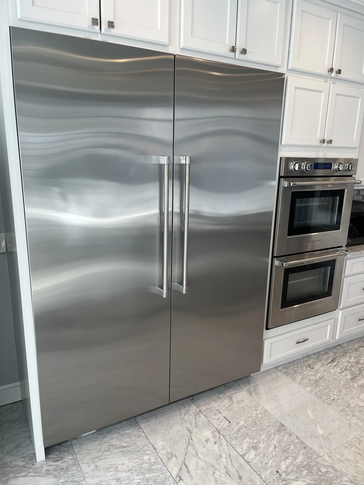 Fisher and Paykel stainless steel built-in refrigerator beside stacked wall ovens