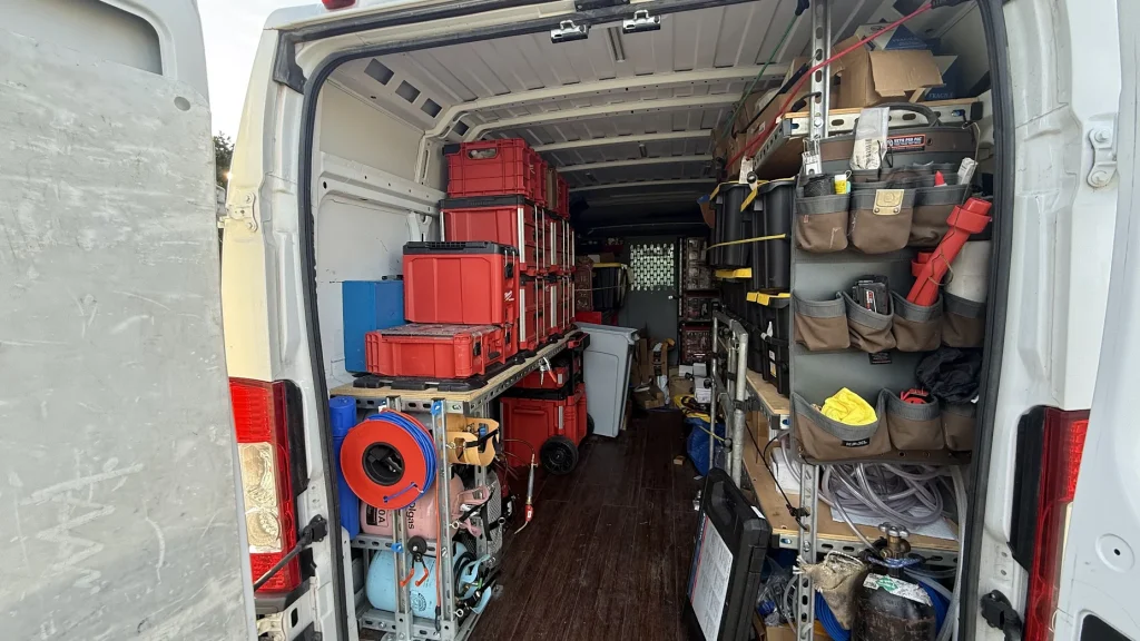 Rear of a service van with organized red tool cases, hoses and parts shelves.