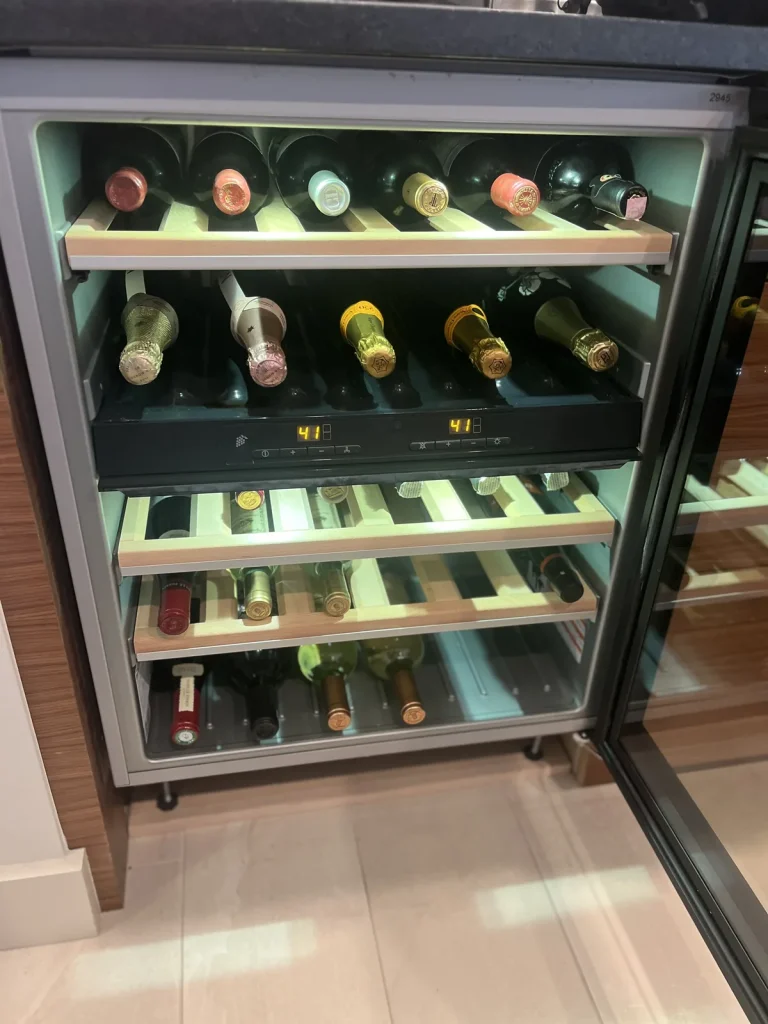 Open wine cooler with wine bottles stored on illuminated slide-out racks