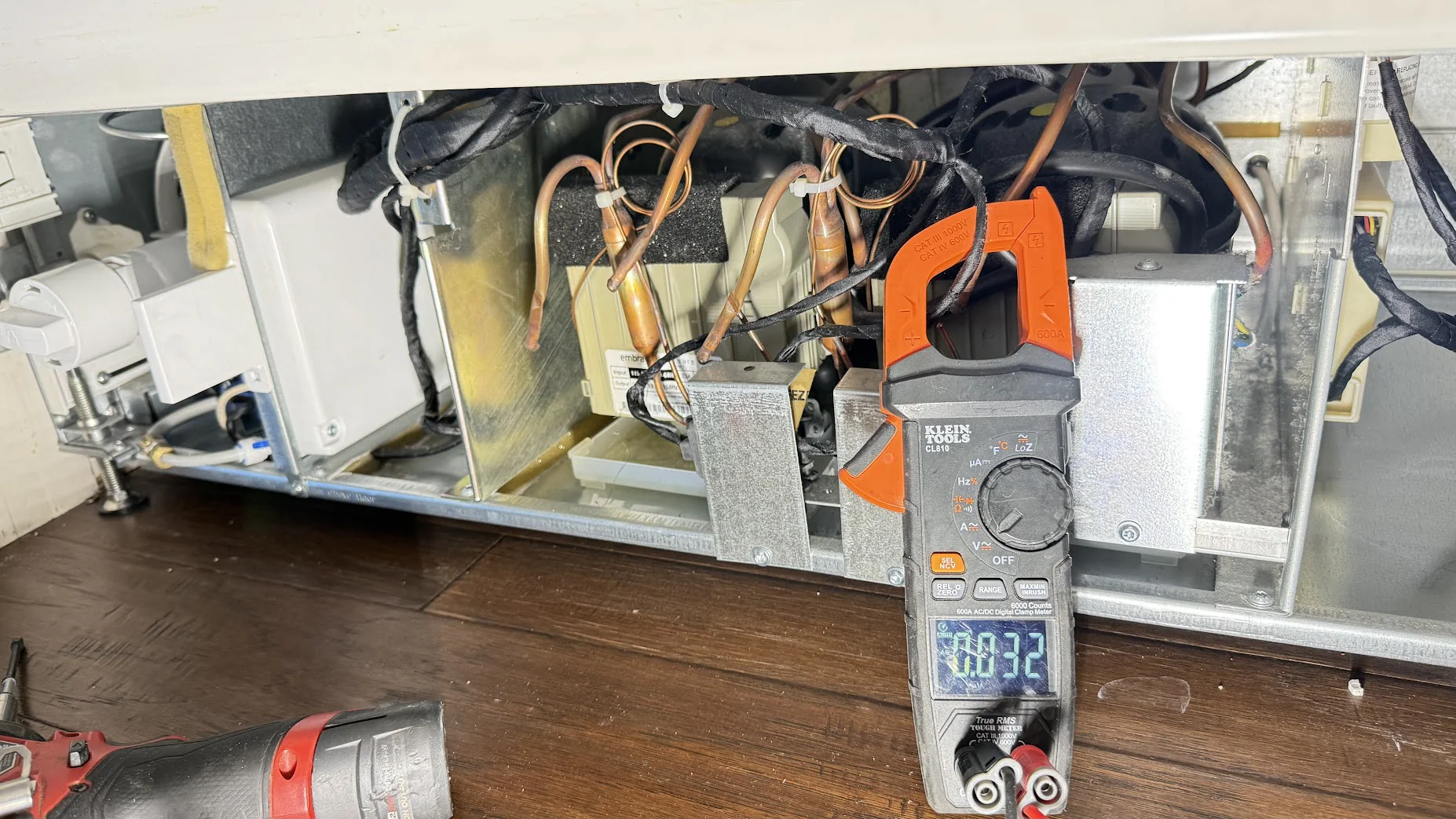 Electrical meter in front of exposed refrigerator wiring and components.