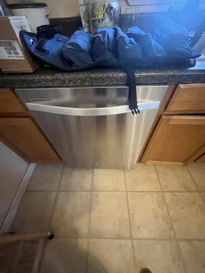 Stainless dishwasher below a counter with repair tools placed above it.