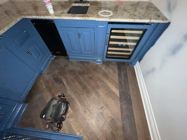 Glass-door undercounter wine cooler installed among blue cabinets.